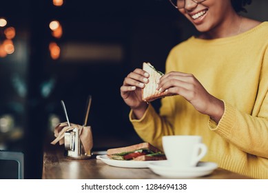 Cropped Photo Of Smiling Woman In Yellow Pullover Sitting In Cafe. She Eating Good Sandwich For Breakfast