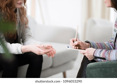 Cropped photo of a therapist writing down notes during therapy with her female patient - Powered by Shutterstock