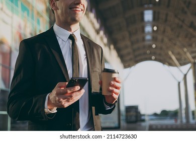Cropped up photo traveler businessman young man in black suit outside at international airport terminal use mobile phone book taxi order hotel hold paper cup drink coffee Air flight business concept.