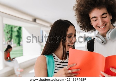 Cropped photo of two students laughing while looking at their notes in the campus