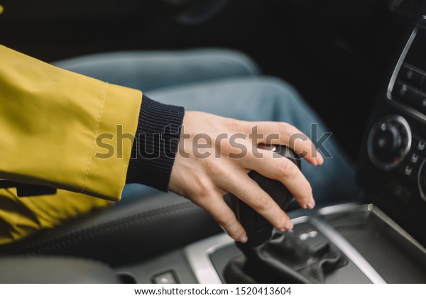 Cropped photo of unrecognizable woman which switches\
gears in the car by hand. Female drive the car. Selective focus.\
Travelling by automobile. Comfort transportation. Journey concept.\
