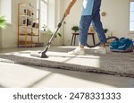 Cropped photo of woman cleaning with vacuum cleaner carpet in the living room at home. Female janitor vacuuming the floor. Cleaning service, housekeeping, housework and household concept.
