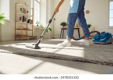 Cropped photo of woman cleaning with vacuum cleaner carpet in the living room at home. Female janitor vacuuming the floor. Cleaning service, housekeeping, housework and household concept. - Powered by Shutterstock