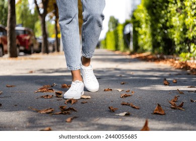 Cropped photo of woman legs in white sneakers going on sidewalk with dry leaves fall season outside - Powered by Shutterstock