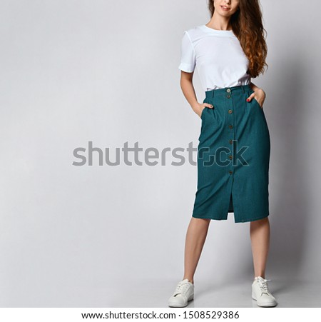 Cropped photo of a young brunette girl with long hair in a white blouse and green skirt. on a light background.