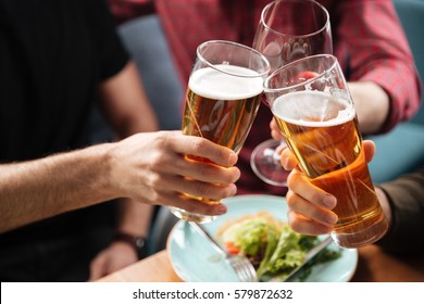 Cropped photo of young friends sitting in cafe while drinking alcohol. Focus on glasses of beer. - Shutterstock ID 579872632