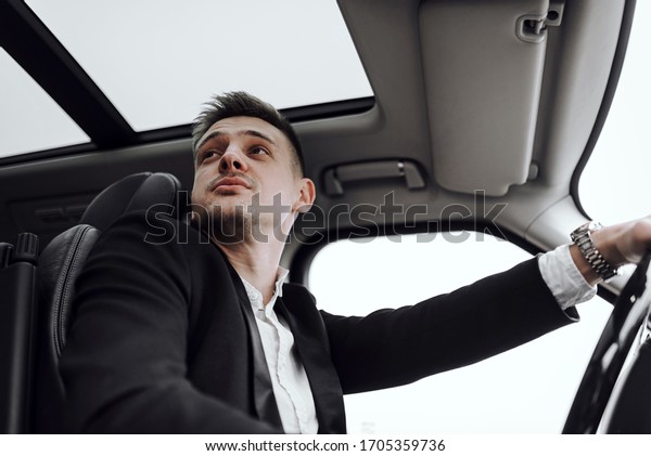 Cropped photo of young handsome man\
looking away while driving car. Rent and trade-in\
concept