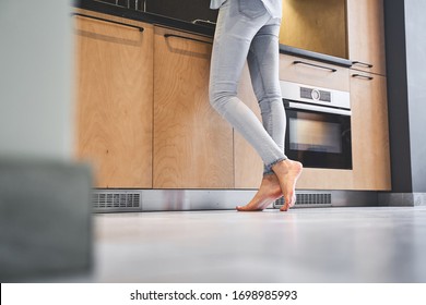 Cropped photo of a young housewife in denim pants standing barefoot on the tile floor - Shutterstock ID 1698985993