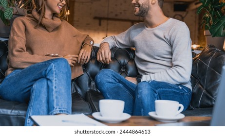 Cropped photo of young male and female businesspeople couple colleagues having a meeting in cafe. Two office workers seats in sofa drinking coffee tea while break in cozy loft hipsters coffee shop. - Powered by Shutterstock