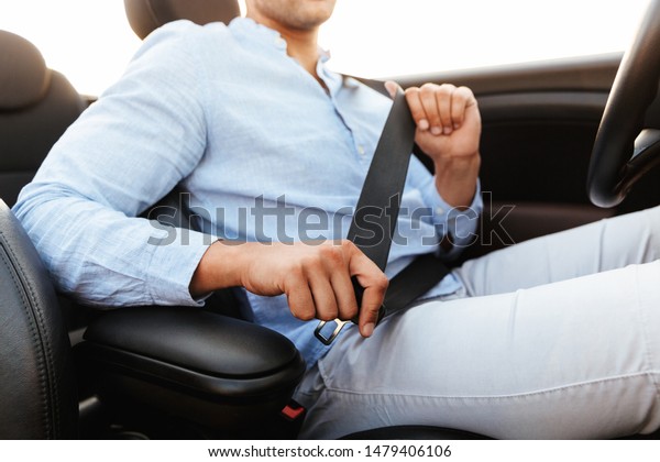 Cropped photo of young man wearing\
seat belt while driving convertible car by seaside at\
sunrise