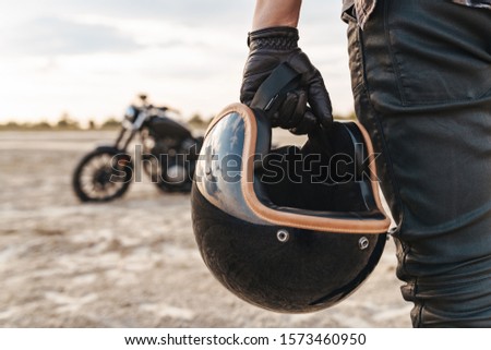 Cropped photo of young strong man biker with helmet outdoors at the desert field.
