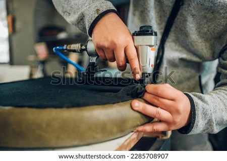 Cropped picture of an artisan's hands using the upholstering tool for making handmade furniture at the furniture workshop. Close up of craftsman using tools at the workshop.