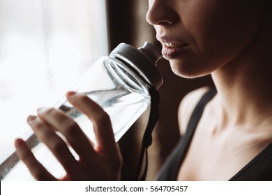 Cropped Picture Of Gorgeous Young Fitness Woman Standing In Gym Near Window While Drinking Water.