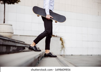 Cropped picture of handsome man in shirt going down the stairs outdoors and holding skateboard under armpit. - Powered by Shutterstock