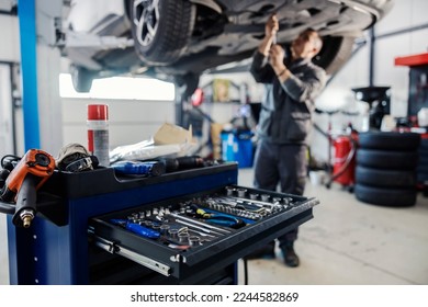 Cropped picture of a mechanic toolbox with tools in drawer with worker repairing car in blurry background at workshop. - Powered by Shutterstock