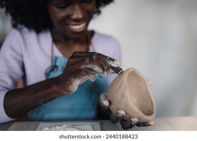 Cropped picture of a multicultural pottery course student sitting in studio and decorating handmade earthenware. Close up of african american woman's hands decorating creative handcraft and pottery. - Powered by Shutterstock