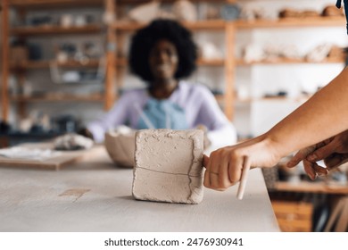 Cropped picture of pottery course tutor's hands cutting clay at ceramics studio. Close up of pottery class instructor using string for clay cutting at pottery workshop. Preparation for pottery class. - Powered by Shutterstock
