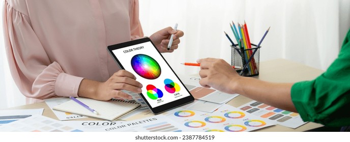 A cropped picture of professional designer selects the color by using color theory and comparing with color wheel on table with designing material and equipment scatter around. Variegated. - Powered by Shutterstock