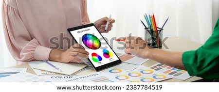 A cropped picture of professional designer selects the color by using color theory and comparing with color wheel on table with designing material and equipment scatter around. Variegated.