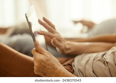 Cropped picture of a senior woman scrolling on tablet in bed. - Powered by Shutterstock