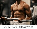 Cropped picture of shirtless muscular multicultural bodybuilder doing biceps curls at gym.