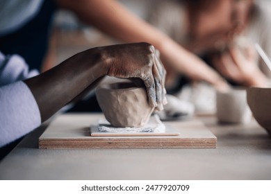 Cropped picture of unrecognizable pottery course attendee learning clay modeling and clay work at ceramics studio. Close up of multicultural pottery class student's hands doing pottery and clay work. - Powered by Shutterstock