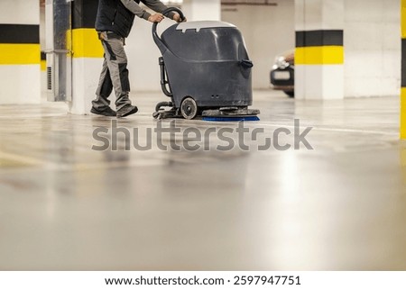 Cropped picture of worker using scrubber machine for washing garage floor.