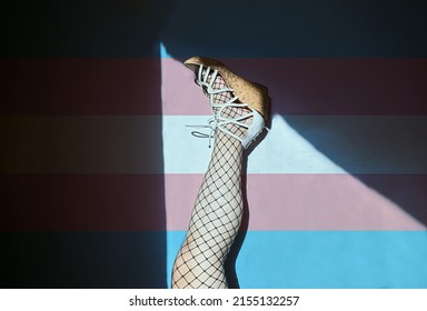 Cropped Portrait Of A 20s Trans Person, Wearing Sandals Lying Down With Legs Raised Isolated On Trans Flag Background.