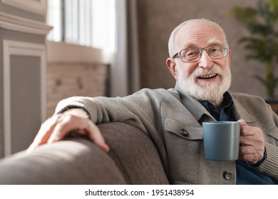 Cropped Portrait Of An Elderly Old Man Drinking Hot Coffee Sitting On The Sofa Indoors. Senior Man In Glasses Enjoying Hot Tea Relaxing In The Living Room