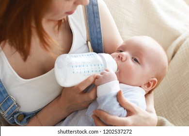 Cropped Portrait Of Intimate Moment Between Mom And Baby. Top View Of Unrecognizable Redhead Female Pressing Toddler Son To Chest And Feeding Him With Infant Formula. Parent And Child In Bedroom