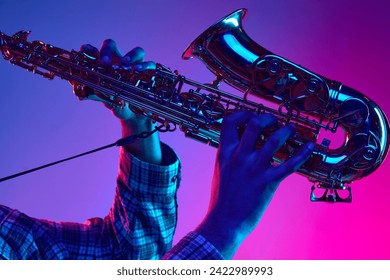 Cropped portrait of jazzman playing saxophone against gradient blue-pink background in neon light. Jazz melodies. Concept of classical musical instrument, concerts and festivals. Ad - Powered by Shutterstock