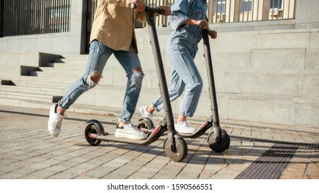 Cropped portrait of legs of couple riding electric scooters along the city street. Modern and ecological transportation concept. Horizontal shot