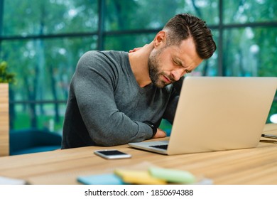 Cropped Portrait Of Nice-looking Young Businessman With Neck Pain Sitting At Office Desk With Laptop