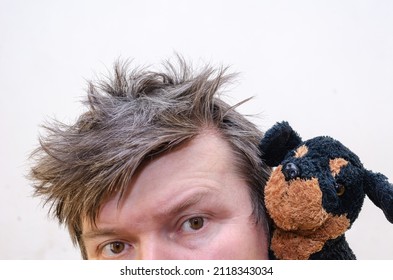 Cropped Portrait of a wriggling man with a puppy toy. A male with ruffled, tangled hair presses his cheek against the stuffed children's toy. Indoors. Selective focus.