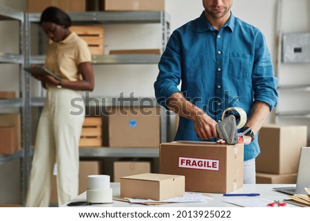Cropped portrait of young man packing boxes at warehouse with Fragile sticker, copy space