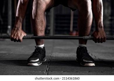 cropped powerful strong african bodybuilder athletic fitness man pumping up abs muscles putting heavy barbell, workout bodybuilding concept. black man during intense training at dark modern gym