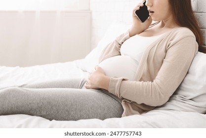 Cropped of pregnant woman is sitting on a bed, engaged in a phone conversation. She appears relaxed and focused as she communicates over the cell phone. - Powered by Shutterstock