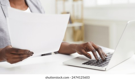 Cropped of professional black woman is handling documents at her desk in an office. The setting is sleek and organized, with a clean desk, contemporary decor - Powered by Shutterstock