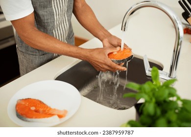 Cropped shot of African American man rinsing ingredients for nutritious salmon dish at kitchen sink indoors, preparing healthy fish meal for dinner in a modern home setting - Powered by Shutterstock