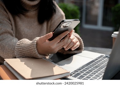Cropped shot of an Asian woman using her smartphone while working remotely at a table outdoors in a garden, chatting or reading an online blog. People and technology concepts