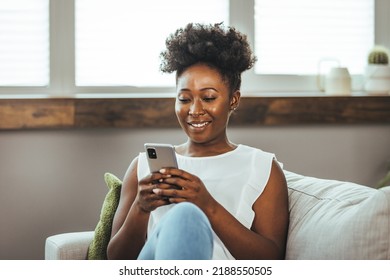 Cropped shot of an attractive young woman using her cellphone while sitting in the living room during the day. Keeping her social media fans updated - Shutterstock ID 2188550505