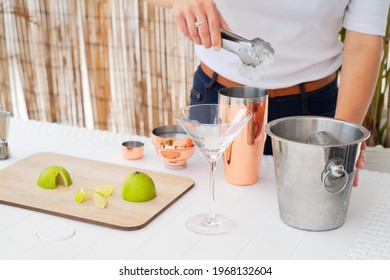 Cropped shot of bartender putting ice cube into shaker, making delicious fresh cocktail with lime juice at bar counter, male barman preparing mojito drink working in outdoor restaurant or summer cafe