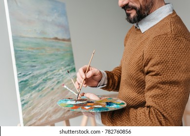 cropped shot of bearded man holding palette and painting on easel at art class  - Powered by Shutterstock