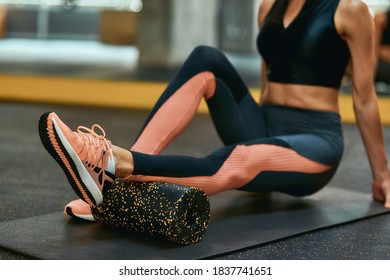 Cropped shot of a beautiful fitness woman in sportswear lying on yoga mat at gym and exercising with foam roller