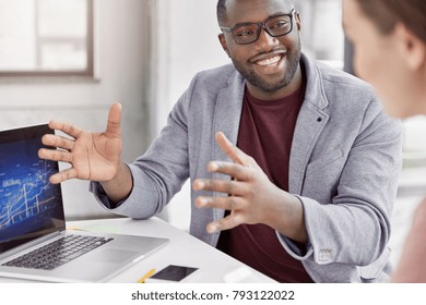 Cropped Shot Of Black Skilled Professional Marketing Expert With Cheerful Expression Makes Speech During Meeting With Business Partner, Explains Presentation And Provides Consultancy In Office