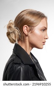 Cropped Shot Of A Blonde Young Woman With A Detachable Chignon On Her Head. The Woman In The Black Jacket With The Detachable Chignon Made Out Of Synthetic Hair Is On A White Background. Side View.