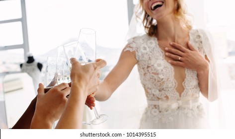 Cropped Shot Of Bride In Wedding Dress And Her Friends Drinking Champagne In Bridal Boutique. Focus On Female Hands Toasting Champagne In Wedding Clothing Shop.