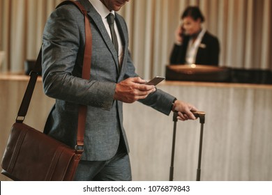 cropped shot of businessman in hotel lobby with mobile phone and luggage. Male business traveler arriving at his hotel, with focus on hands holding smart phone. - Powered by Shutterstock