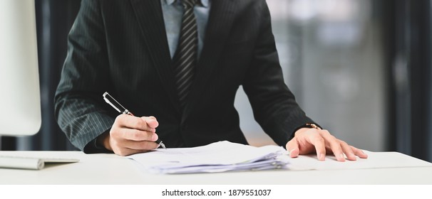 Cropped Shot Of Businessman In Suit Hand Holding Pen Filling Paper Business Document Or Signing Contract At Office Desk.