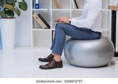 cropped shot of businessman working with laptop while sitting on fit ball - Powered by Shutterstock